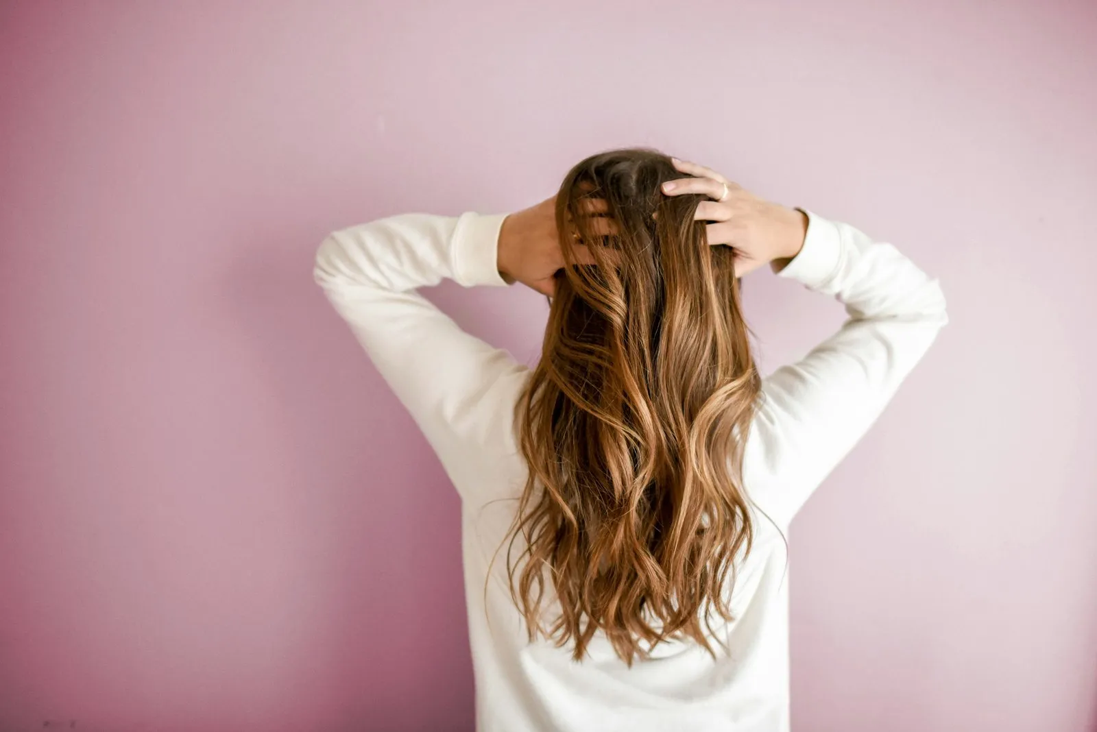 Donna di spalle con lunghi capelli mossi davanti a una parete rosa